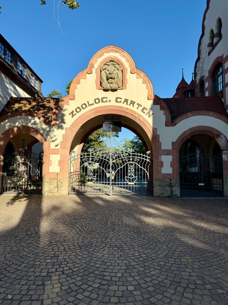 Zoo Leipzig, Tierpark, erholung Eingangstor mit "Historische Schule" Schriftzug und schönen Pflanzen im Hintergrund.