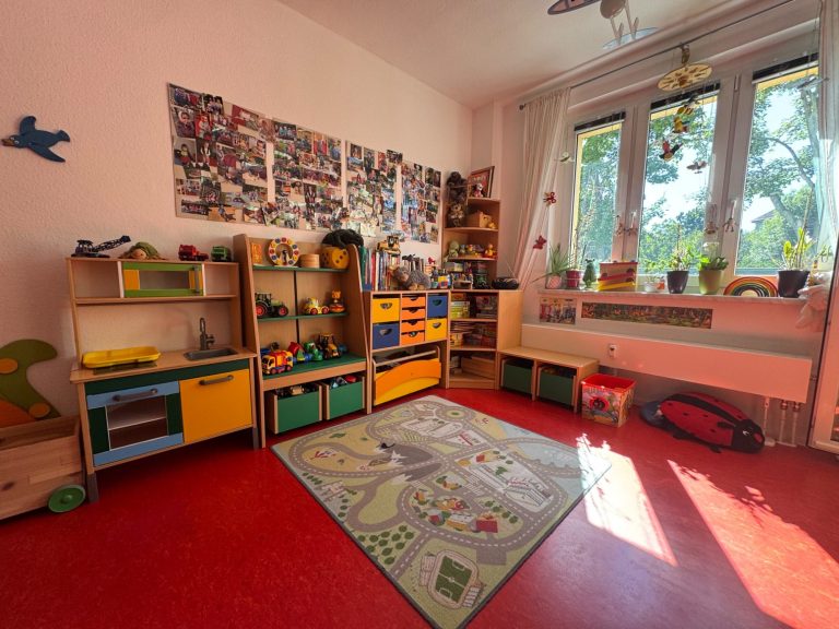 Spielzimmer Bunter Spielbereich mit Regalen, einem Teppich und großen Fenstern.