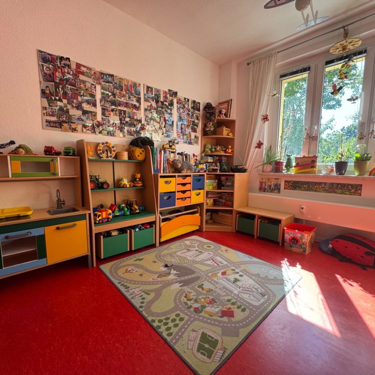 Bunt eingerichteter Kinderraum mit Spielzeug, Teppich und großen Fenstern.